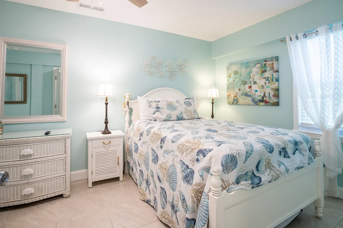 This interior image features a calming bedroom with ocean-themed bedding, colorful artwork, soft lighting, and sunlight pouring through the windows. The peaceful, inviting ambiance highlights the relaxing retreat awaiting couples after a day of exploration.