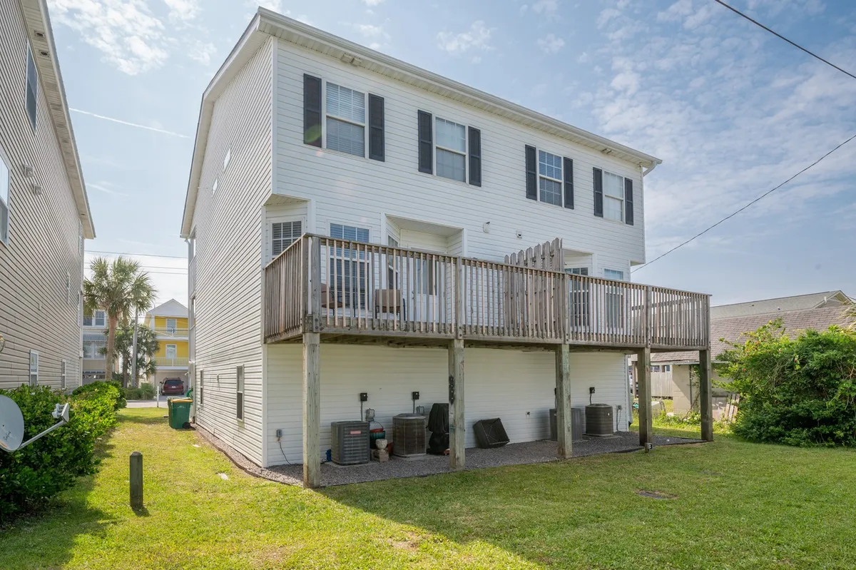 A view of a deck with outdoor seating, overlooking a grassy lawn. The yard is open and sunlit, suggesting space for gatherings, picnics, or play. This scene radiates a relaxed, coastal vibe, ideal for casual outdoor enjoyment.