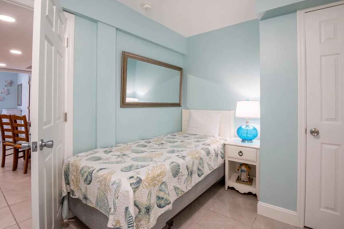 A cozy single bed adorned with a decorative quilt, accompanied by a blue lamp and a mirror. The intimate setup suggests a perfect space for solo travelers to rest, reflect, or read in a peaceful environment.