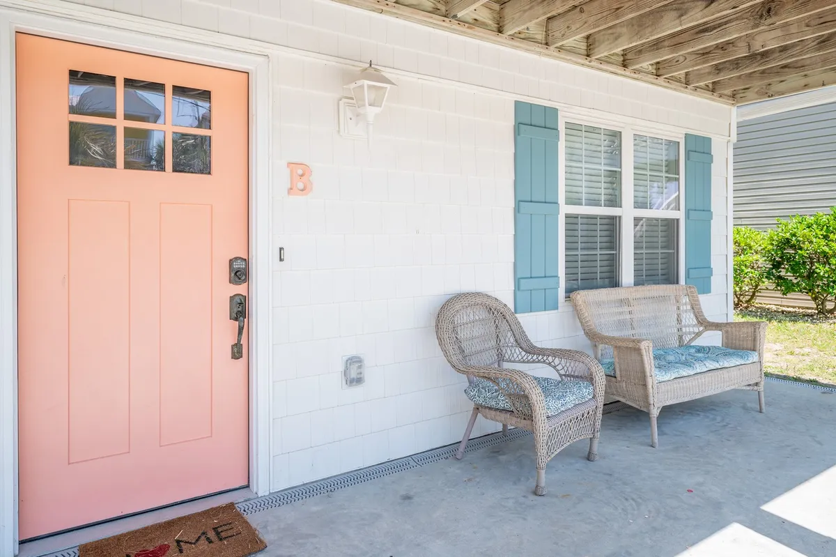This image shows a peach-colored front door flanked by blue shutters, with wicker chairs placed on a welcoming front porch. The setup suggests an inviting entry point and provides a clear view of a comfortable outdoor seating area, ideal for relaxing or enjoying your morning coffee.