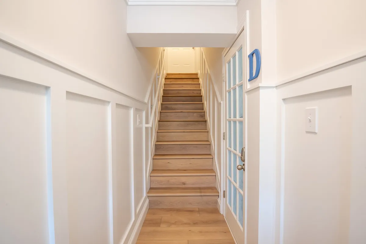 An open, inviting staircase with plenty of natural light, a glass door, and crisp white walls. The scene conveys movement between floors and the spaciousness within the home, suggesting multiple interconnected levels.
