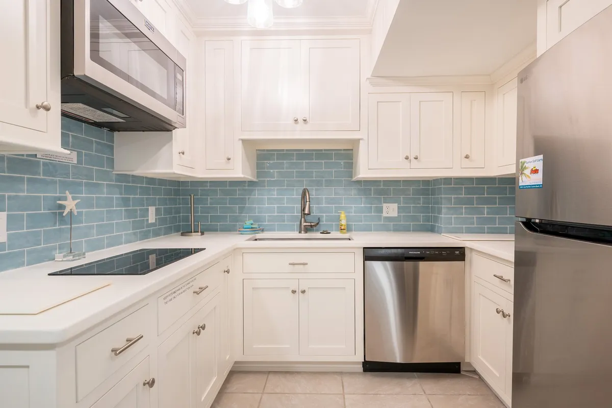 A cheerful, modern kitchen featuring a light blue backsplash, stainless steel appliances, and white cabinetry. The space is bright and inviting, designed for cooking, entertaining, or gathering with family and friends.
